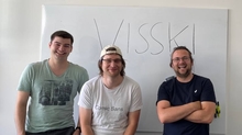 Kai, Tom and Robert smiling in the camera in front of a whiteboard with "WissKI" written on it.